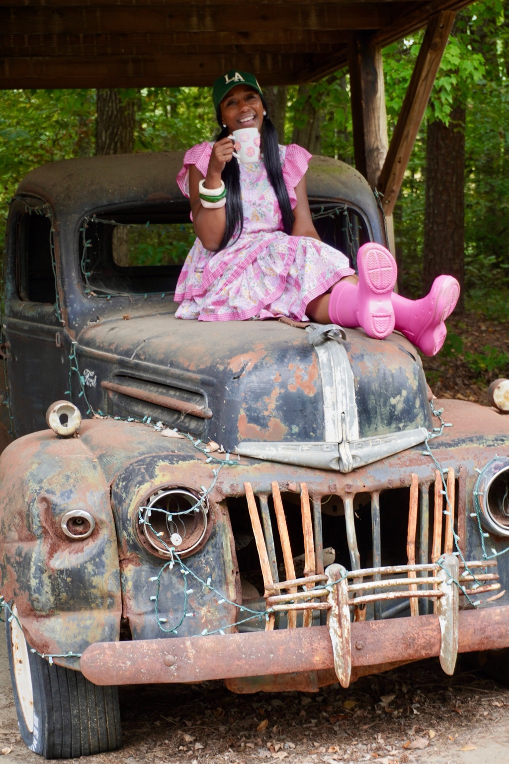 Founder Latasha Nesbit smiling with a coffee mug while seated on a vintage car in her pink outfit